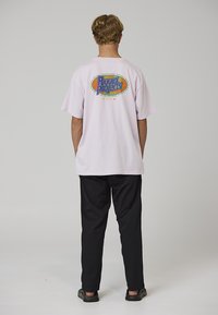 Světle růžové oversized tričko s vícebarevným potiskem na zádech, kombinované s černými kalhotami a tmavými slip-on botami.