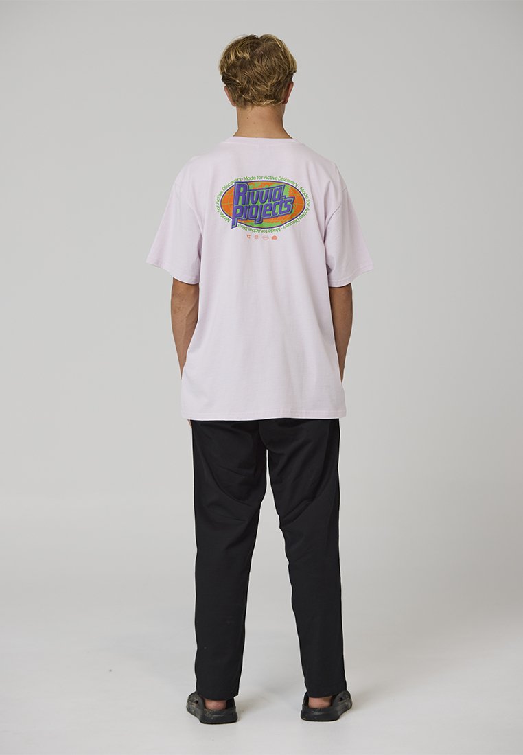 Světle růžové oversized tričko s vícebarevným potiskem na zádech, kombinované s černými kalhotami a tmavými slip-on botami.