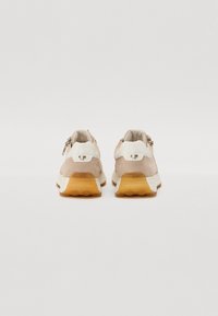 Baskets en suède beige avec un accent en cuir blanc et une semelle en caoutchouc, dotées d'une fermeture éclair à l'arrière et d'un talon texturé contrastant.