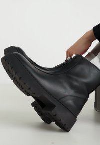 Botas de cuero negras con suela de goma gruesa, con un zipper lateral y superficie texturizada, situadas sobre un fondo blanco.