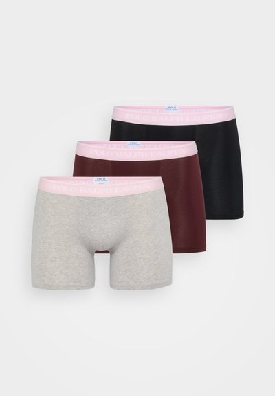 Tris vyriškų trumpikių poros, kurios yra pilkos, bordo ir juodos spalvos. Kiekvienos juosmens juosta yra minkšta rožinė, su "POLO RALPH LAUREN" prekių ženklu.
