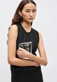 Zwarte mouwloze gebreide top met een gestructureerd patroon en kleine pailletten, gecombineerd met een transparante clutch met een zilverkleurig metallic accent.