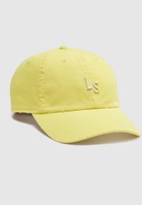 Κίτρινο καπέλο του μπέιζμπολ με φθαρμένες άκρες και κεντημένα γράμματα "LS" στο μπροστινό μέρος, εμφανιζόμενο σε ένα απλό φωτεινό φόντο.