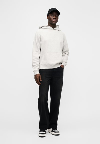 Šedá mikina s kapucí a přední kapsou, doplněná tmavými džínami a černo-bílými teniskami. Baseballová čepice má logo.