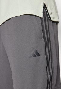 Gray athletic shorts made of textured fabric, featuring three black stripes along the side and a black Adidas logo on the thigh.