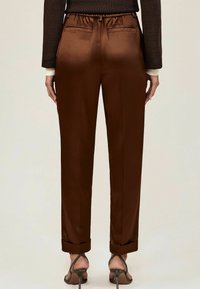 Barna selyem nadrág rugalmas derékkal, sima egyenes lábakkal, felgöngyölt nadrágszárakkal és két hátsó zsebbel. A fényes textúra kiemeli a dizájnt.
