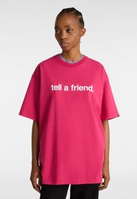 Overdimensioneret t-shirt med korte ærmer i lys pink bomuld med hvid tekst "fortæl en ven." Rund halsudskæring og afslappet pasform.