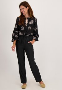 Zwarte blouse met wit paisleymotief, lange mouwen, ronde zoom, gecombineerd met zwarte broek en beige geweven instappers.