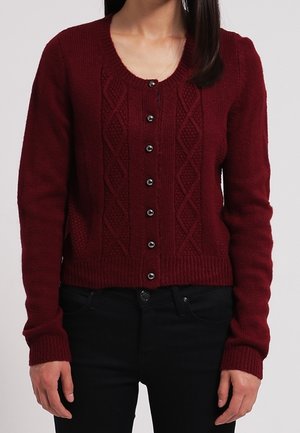 Cardigan tricoté bordeaux avec un motif en losanges, ourlet et poignets côtelés, et boutons noirs sur le devant. Porté sur un pantalon sombre.