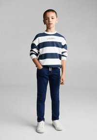 Námořnicky modrý a bílý pruhovaný svetr s textem, v kombinaci s tmavými džíny a bílými teniskami. Střih je volný, s kulatým výstřihem a dlouhými rukávy.