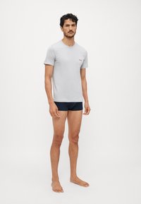 Lys grå bomull t-skjorte med rund hals og liten rød "HUGO" logo, kombinert med marineblå shorts. Enkel, tettsittende design.