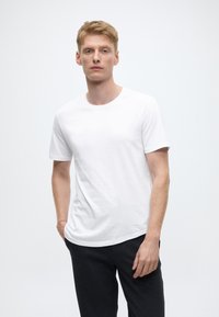 Maglietta bianca in cotone con maniche corte e scollo rotondo, abbinata a pantaloni grigio scuro. Design semplice, texture liscia, senza motivi.