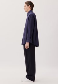 Marineblaues Langarmshirt mit lockerer Passform, kombiniert mit schwarzen weit geschnittenen Hosen und weißen Sneakers, im Profil vor einem neutralen Hintergrund gezeigt.