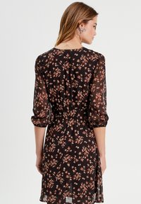Robe noire à motifs floraux avec de longues manches transparentes, taille élastique et jupe fluide. Petit motif floral rose et blanc sur l'ensemble.