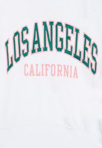 Fehér pulcsi, oversized "LOS ANGELES" zöld hímzéssel és "CALIFORNIA" rózsaszín hímzéssel. Simaság és bordázott alj jellemzi.