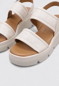 Sandalias de plataforma blancas con dos correas anchas. Parte superior de cuero suave, plantilla marrón y suela gruesa con un agarre texturizado. Diseño minimalista.