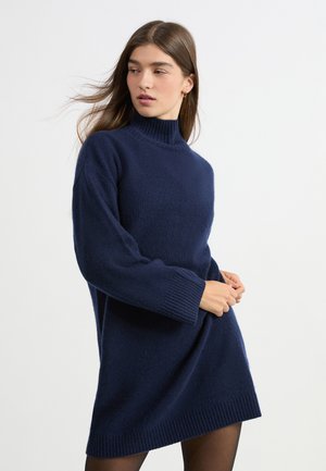 Granatowa sukienka sweterkowa z golfem, wykonana z miękkiej, teksturowanej tkaniny, z prążkowanymi mankietami i dołem, o luźnym kroju oraz długich rękawach.