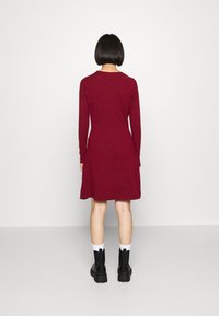 Burgundy pitkähihaista mekkoa, jossa on levenevä helma, valmistettu pehmeästä kankaasta. Yhdistettyinä mustien näyttävien saappaiden ja valkoisten sukkien kanssa, nähtynä takaa.