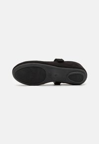 Scarpa slip-on in suede nero con suola in gomma testurizzata, dotata di una piccola cinghia per la regolazione. La parte inferiore presenta un battistrada per una presa migliore.