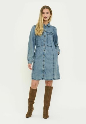 Heledast sinisest teksariidest kleit-särk, millel on eest nööpidega avamine, rinnatasku, pikad varrukad ja küljetaskud, kantud pruunide põlveni ulatuvate saapadega.