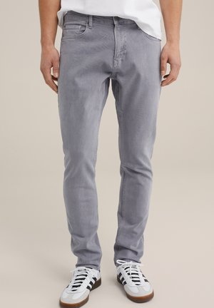 Jean en denim gris avec une coupe slim, ayant une texture lisse. Ils disposent de cinq poches et sont associés à des baskets blanches.