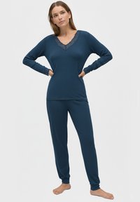 Conjunto de ropa de casa en azul marino que incluye una parte superior de manga larga con escote en V de encaje y pantalones ajustados a juego, hechos de una tela suave y texturizada.