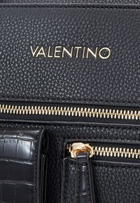Svart läderhandväska med texturerad yta, guldfärgade dragkedjor och "VALENTINO"-logotyp i guld. Inkluderar en accent i krokodilsmönster.