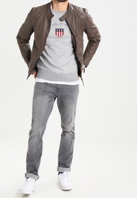 Braune Lederjacke, grauer Sweatshirt mit Logo, graue Jeans und weiße Sneaker. Lässiges Outfit mit tailliertem Design und hochgeschlagenen Ärmeln.