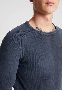 Maglione a coste blu navy con scollatura rotonda e un design texturizzato e aderente. Presenta spalle senza cuciture e tessuto morbido per il massimo comfort.