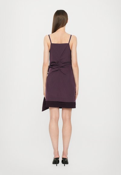 Purple sleeveless dress with a ruched back detail, knee-length, featuring a layered hem design and worn with black high heels.