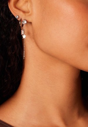 Gouden oorbellen met hoepels en studs, versierd met heldere en roze edelstenen, en een hangende zilveren ketting met een ster bedel.