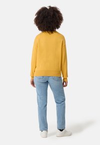Maglione giallo a maglia con vestibilità morbida e orlo a costine, abbinato a jeans in denim azzurro chiaro e sneakers bianche. Vista posteriore.