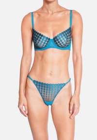 Ensemble de lingerie turquoise avec des détails en maille transparente et broderie circulaire. Le soutien-gorge est souple avec armatures et bretelles ajustables. Le string présente un design similaire.