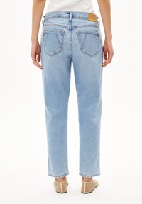 Vaaleansiniset farkut, joissa on suora lahkeen malli, viisi taskua ja pieni ruskea etiketti takana vyötärönauhan kohdalla. Sileä pinta.