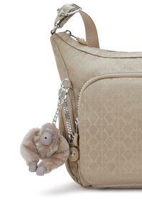 Beige axelväska med geometriskt mönster, slät yta, dragkedjefickor och en lurvig apcharm fäst med en silverkedja.
