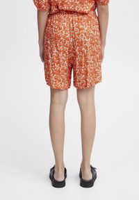Rode en witte bloemenprint shorts met een elastische tailleband, geplooide details en een relaxte pasvorm. Draagt met zwarte instapschoenen.
