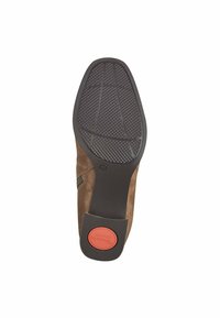 Suela de zapato de ante marrón que presenta un patrón de agarre de goma negra texturizada con un acento circular rojo marcado como "Comodidad". Bordes suaves y forma redondeada.