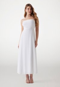 White maxi dress with thin straps, fitted bodice, and flowing skirt. Designed with a smooth texture and subtle seam details.
