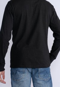 Pitkähihaisessa mustassa paidassa on rento istuvuus ja se on valmistettu pehmeästä materiaalista. Parina vaaleansiniset farkut, joissa on hienovaraisia ompeluyksityiskohtia taskuissa.