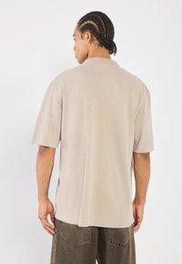 Beige shirt met korte mouwen, relaxed fit, zachte textuur, afklapbare kraag en minimalistisch ontwerp. Aanzienlijke achternaad detail.
