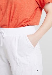 Shorts blancs avec poches, en tissu léger, associés à un T-shirt orange. Le T-shirt a une coupe décontractée et des manches courtes.