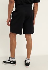 Svarta träningsshorts med elastiskt midjeband och sidofickor, parats med svarta lågt skurna sneakers och vita randiga strumpor.