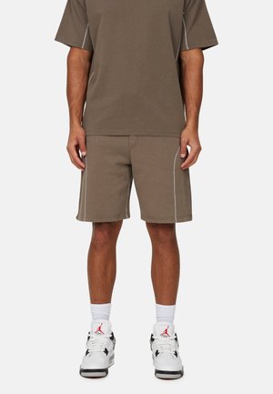 T-shirt en coton marron et shorts assortis avec des coutures blanches, associés à des baskets blanches et noires et des chaussettes blanches mi-mollet.