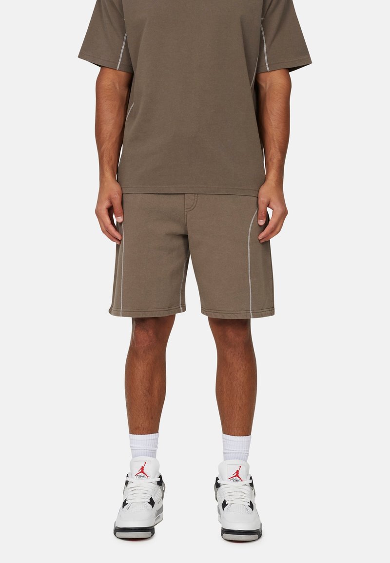 Bruine katoenen t-shirt en bijpassende shorts met witte stiksels, gecombineerd met witte en zwarte sneakers en witte crew-sokken.