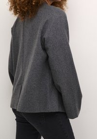 Graue Wollmischung Jacke mit strukturiertem Design, Schulternähten und weiten Ärmeln; kombiniert mit dunklen Jeans, von hinten gezeigt.