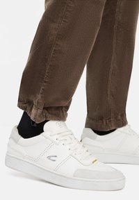 Hvide lædersneakers med grå ruskind detaljer, der har perforerede elementer, flade snørebånd og en tekstureret gummisål. Båret med brune fløjlsbukser.