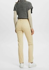 Pantalones beige claros con un diseño de pierna recta, que cuentan con dos bolsillos traseros y costuras sutiles. Combinados con un suéter de punto gris.