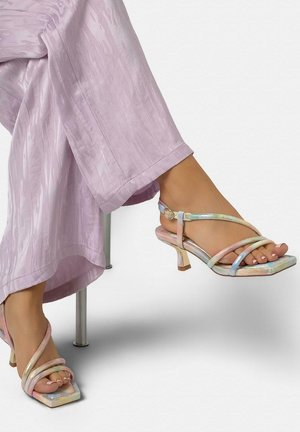 Jambes croisées portant un pantalon large texturé lilas et des sandales à talons à brides pastel iridescentes avec des bouts carrés.