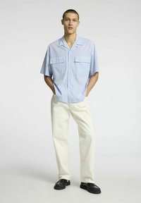 Šviesiai mėlynos ir baltos languotos trumpomis rankovėmis marškiniai su mygtukais, turintys dvi priekines kišenes. Dėvimi su kreminės spalvos kelnėmis ir juodais batais.