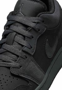 Κοντινή λήψη μαύρου αθλητικού παπουτσιού Nike που δείχνει υφασμένα κορδόνια, πάνελ από σουέτ και δέρμα, διάτρητη μύτη και ραμμένο λογότυπο swoosh στο πλάι.